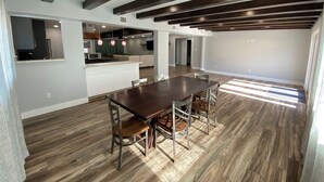 Ampla sala de estar com mesa de jantar, cozinha e teto alto com vigas aparentes.
