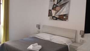 A modern bedroom with a bed, bedside tables, a wall-mounted abstract art piece, and a window with curtains. - YOUR HOUSE (Olbia)