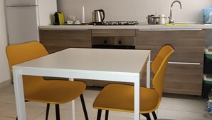 A modern kitchen with a white table, two yellow chairs, a grey sofa, and a stainless steel range hood. - YOUR HOUSE (Olbia)