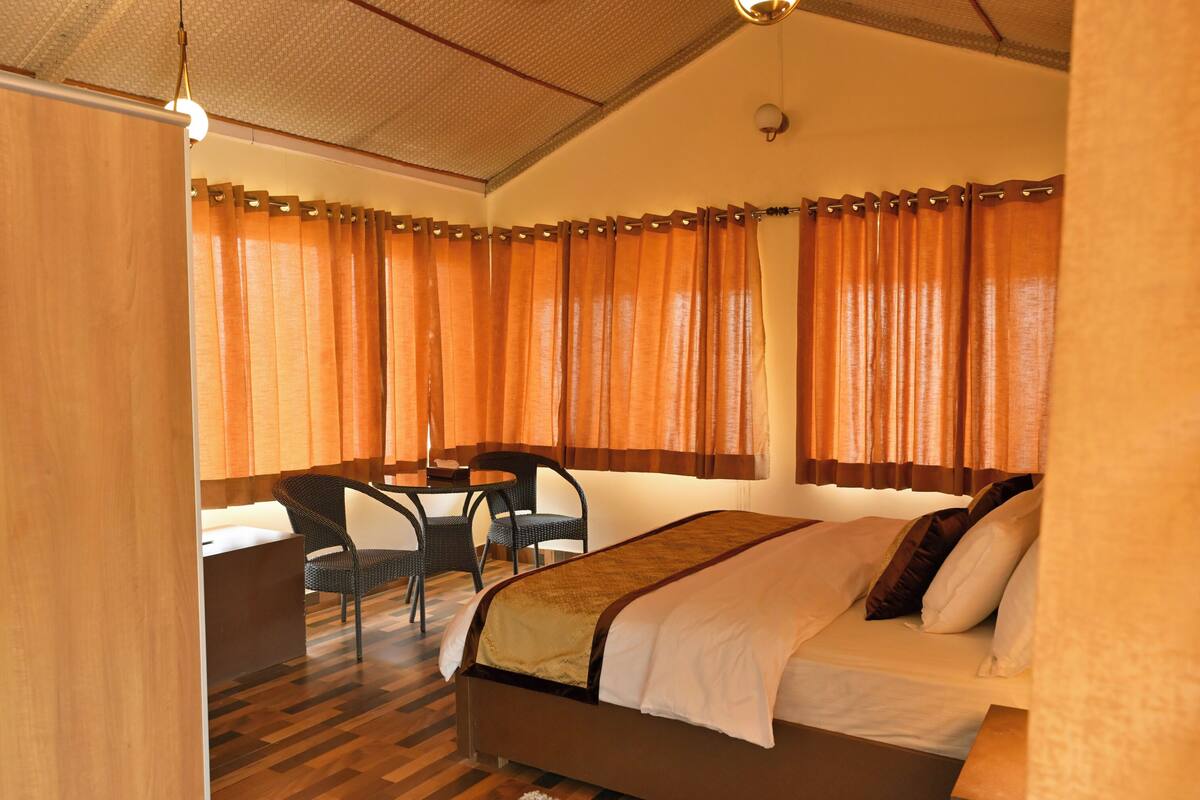 A hotel room with a bed, a desk, two chairs, and a window with curtains.