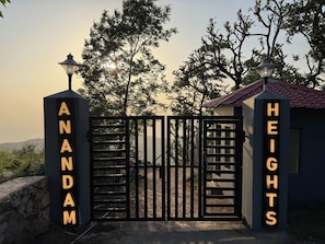 A gated entrance with 'ANANDAM' and 'HEIGHTS' signs, a stone wall, and trees in the background. - Anandam Heights (Vikasnagar)