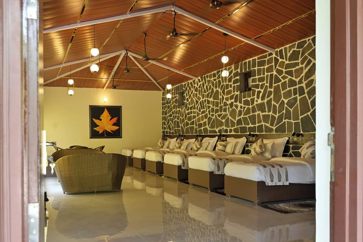 A hotel room with a stone wall, a large maple leaf artwork, a long row of beds, and a ceiling with wooden beams and hanging lights.