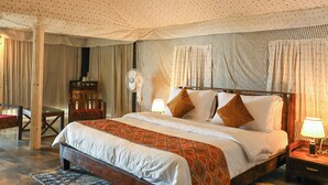 Un dormitorio con cama, mesita de noche, lámpara, cortinas y un ventilador.