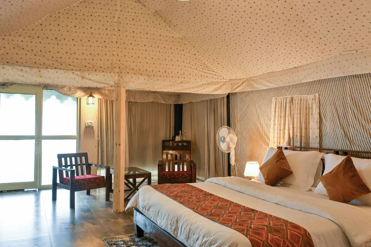 A bedroom with a bed, a chair, a desk, a fan, and curtains.