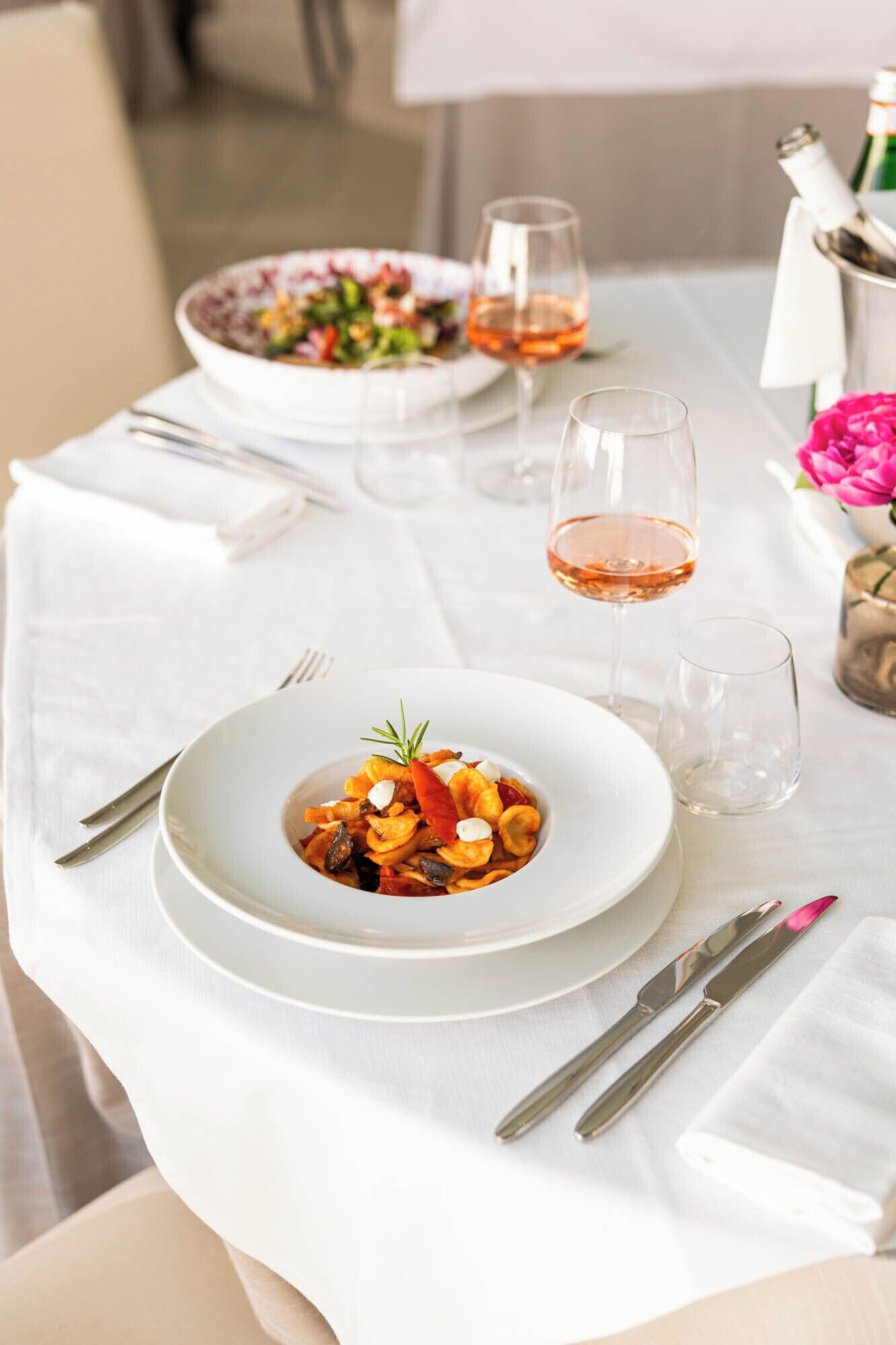 A dining table with plates of food, glasses of wine, and cutlery.
