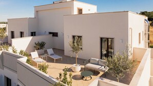 A modern rooftop terrace with white walls, a seating area with lounge chairs and a table, and potted plants. - ARBORIS BELLI HOTEL  (Alberobello)