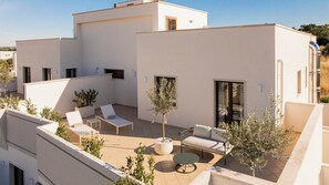 A modern rooftop terrace with white walls, a seating area with lounge chairs and a table, and potted plants. - ARBORIS BELLI HOTEL  (Alberobello)