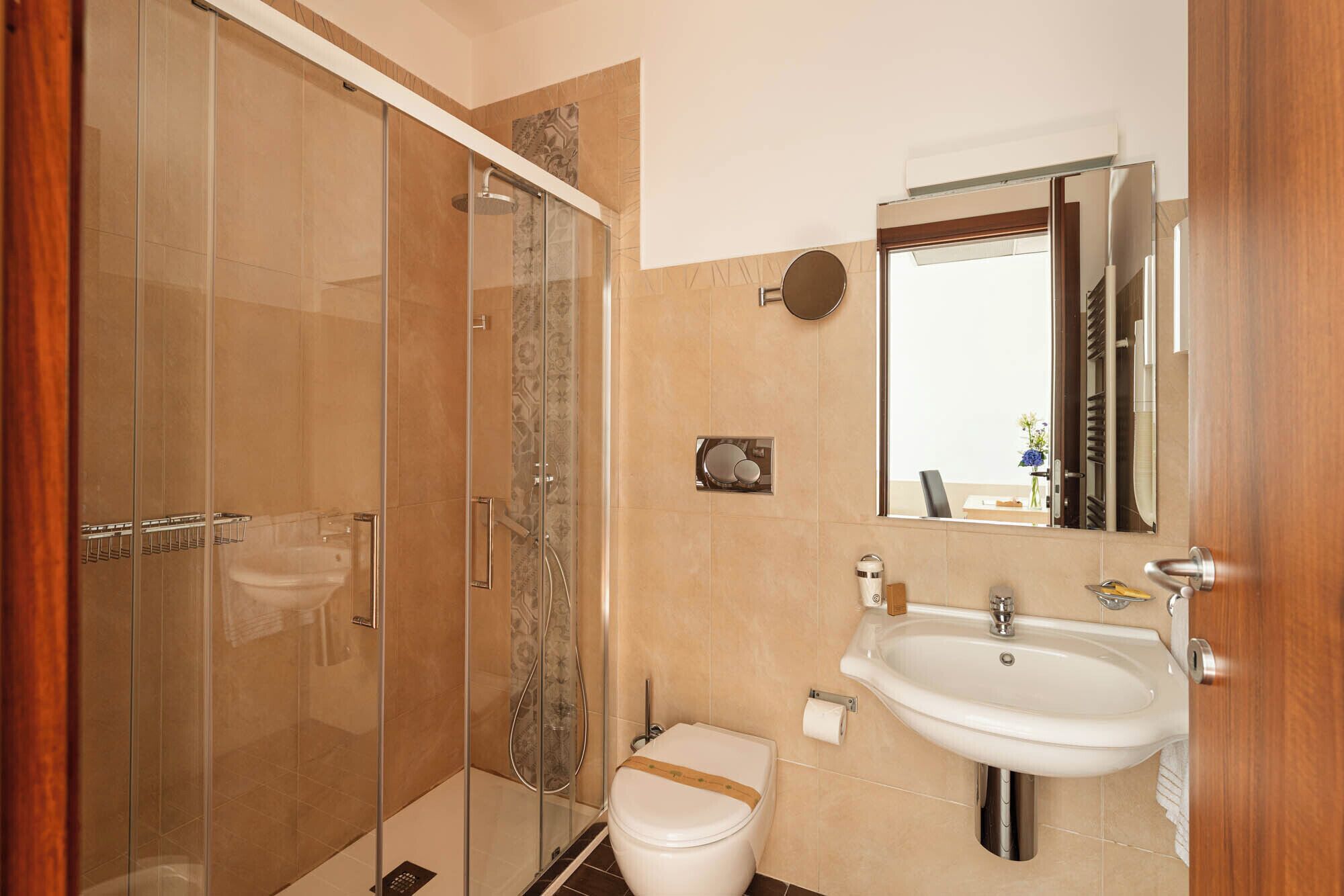 Een badkamer met een douche met glazen wand, een toilet, een wastafel en een spiegel.