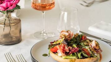 Une table à manger avec une assiette de nourriture, deux verres à vin et un vase avec une fleur.