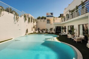 A swimming pool with lounge chairs and a building with a sign in the background. - ARBORIS BELLI HOTEL  (Alberobello)