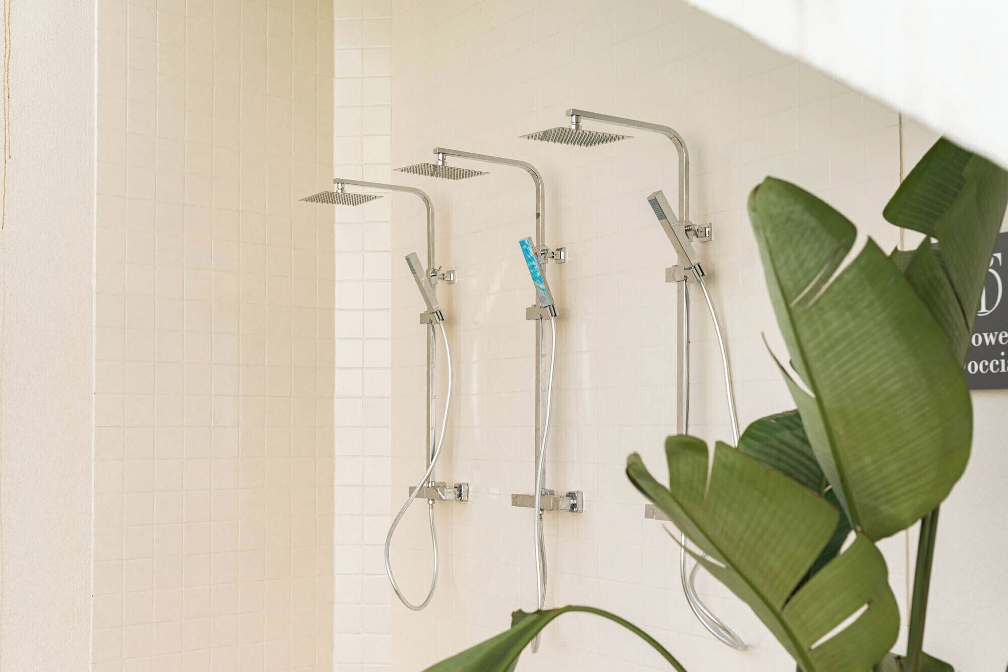 A bathroom with three showerheads and a tiled wall.