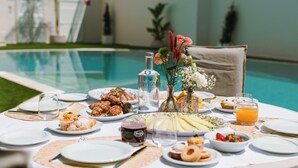 A dining table set for breakfast with various dishes, a bottle, and a glass of orange juice by a poolside. - ARBORIS BELLI HOTEL  (Alberobello)