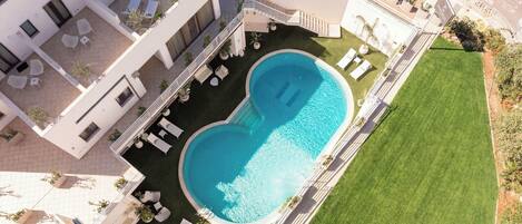 A modern hotel with a rooftop pool, outdoor seating, and a well-maintained lawn.