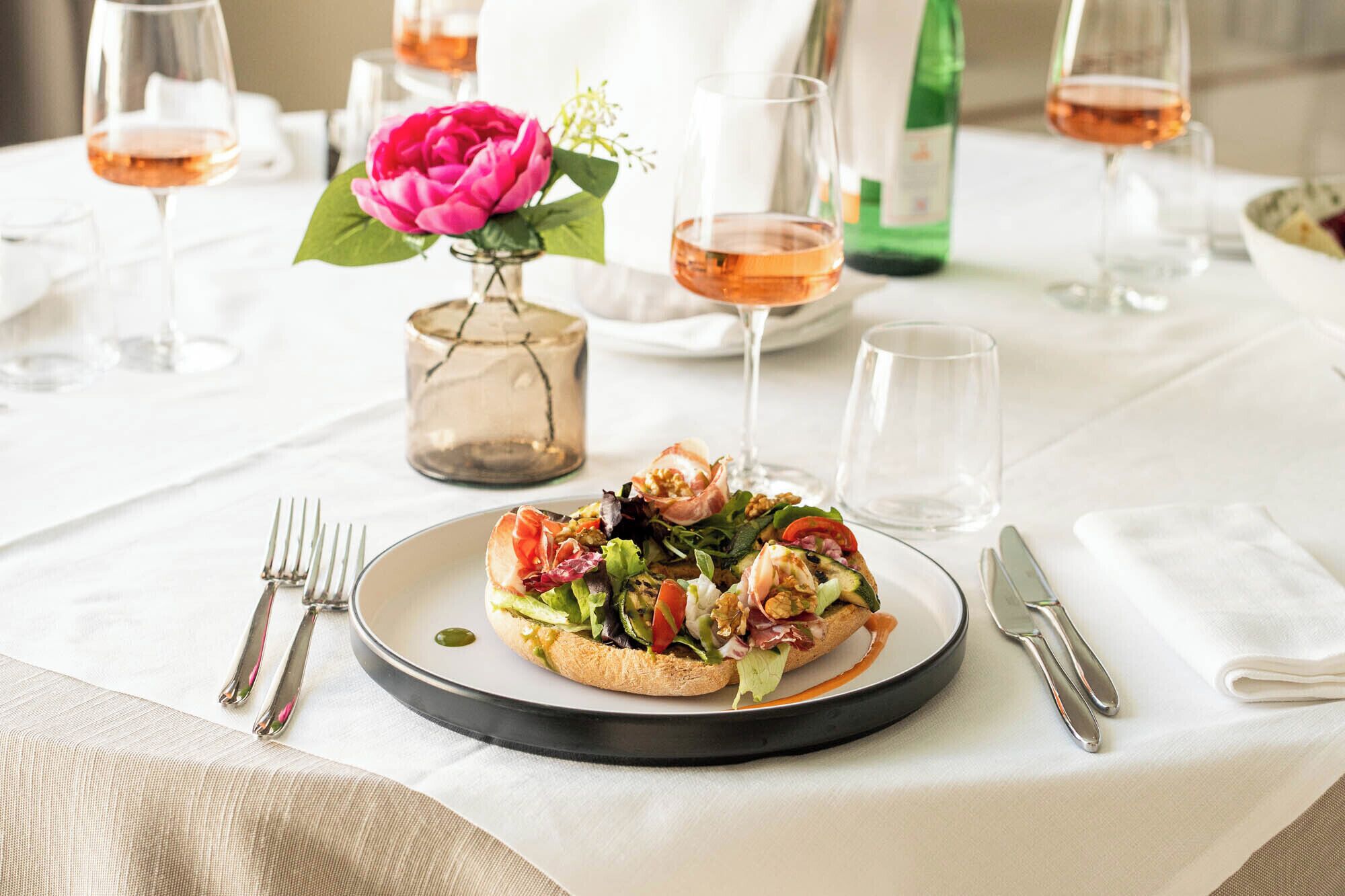 Una mesa de comedor con un plato de comida, copas de vino y cubiertos.
