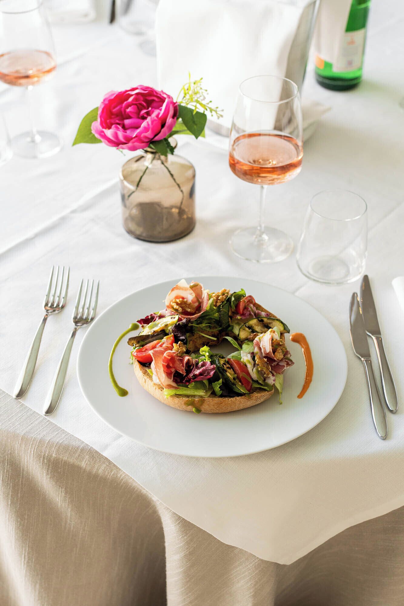 Een eettafel met een bord eten, een glas wijn en een vaas met een bloem.