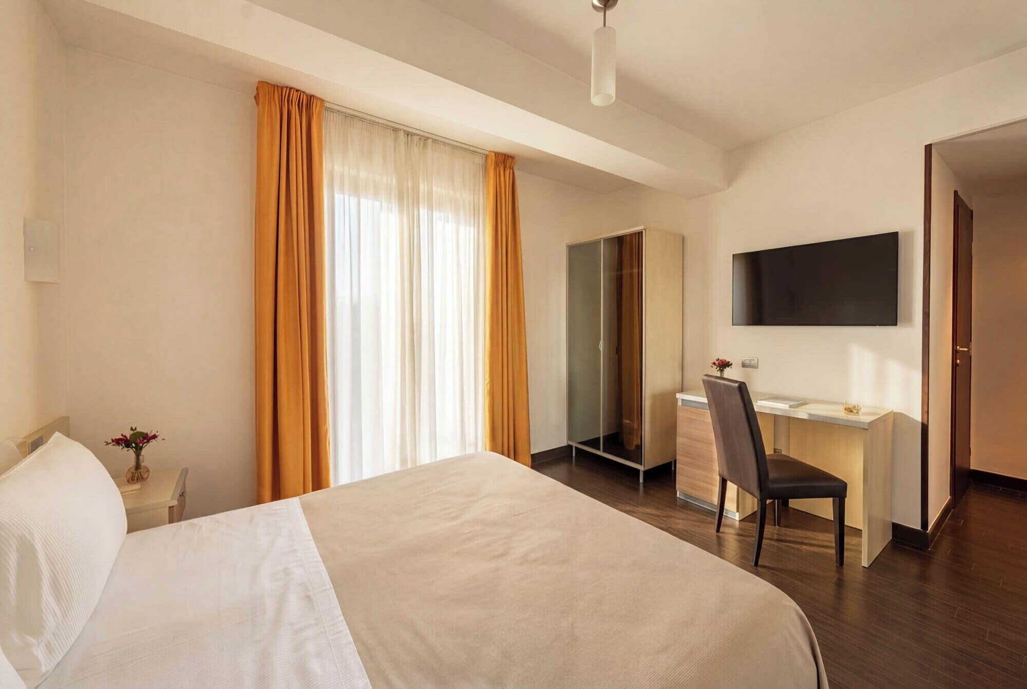 Una habitación de hotel con cama, escritorio, silla, televisor y armario.