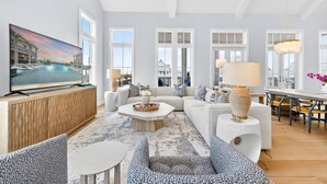 A spacious living room with a large TV, comfortable seating, a dining area, and large windows. - Bay Views, 3 King Suites & Ultimate Kids Retreat @CinnamonShore (Port Aransas)