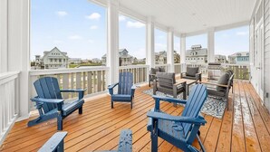 A covered outdoor deck with Adirondack chairs, a table, and a grill. - Bay Views, 3 King Suites & Ultimate Kids Retreat @CinnamonShore (Port Aransas)