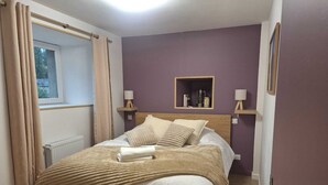 Ein ordentlich bezogenes Bett mit einer beige farbenen Decke, einem hölzernen Kopfteil und zwei Nachttischlampen.