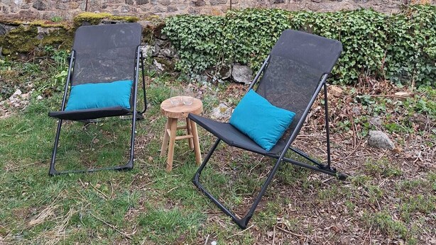 Zwei Lounge-Sessel mit blauen Kissen, ein kleiner runder Holzschemel und eine Steinmauer mit Grünpflanzen.