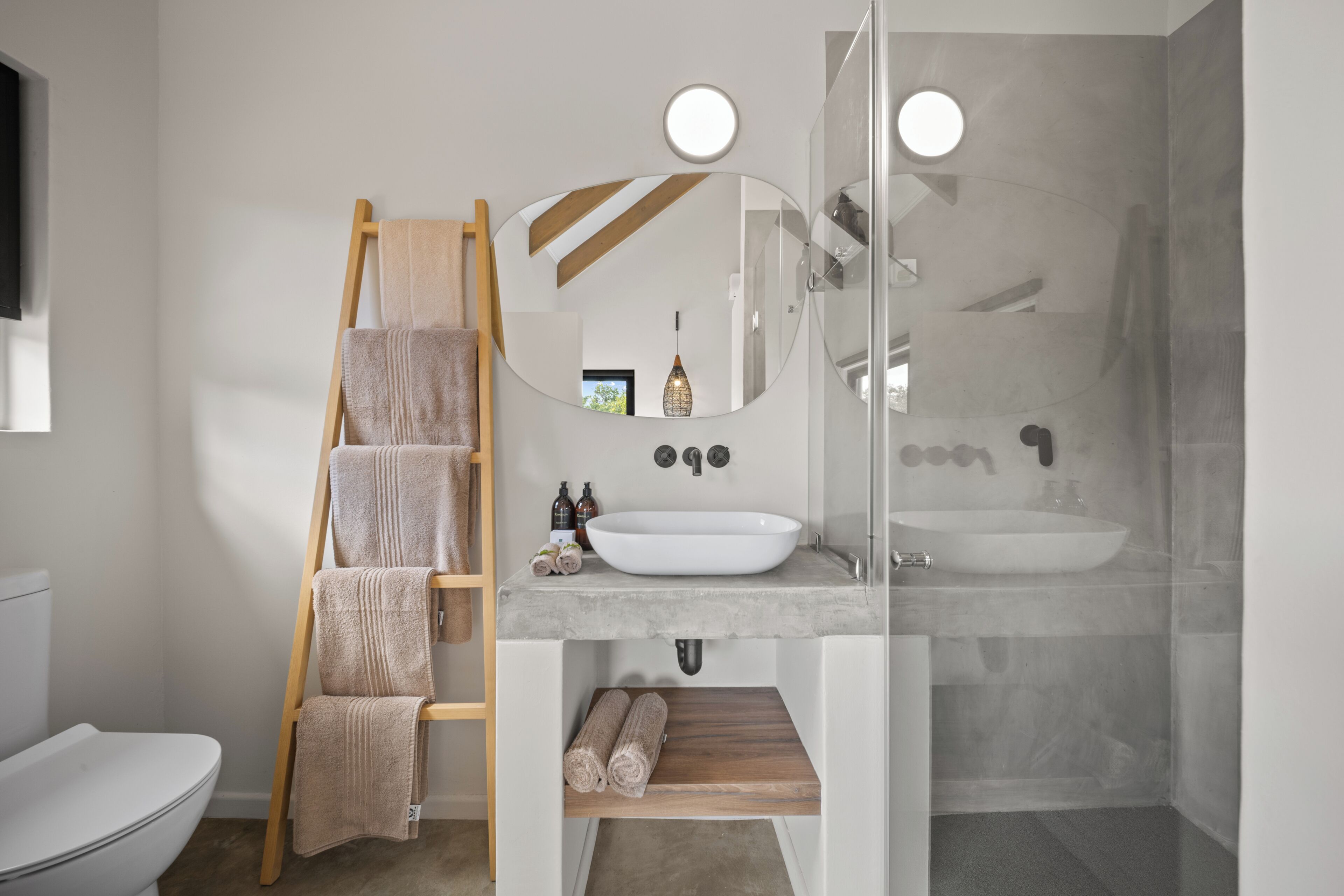 Un baño moderno con un toallero de madera, un espejo grande, un lavabo blanco y una cabina de ducha de vidrio.