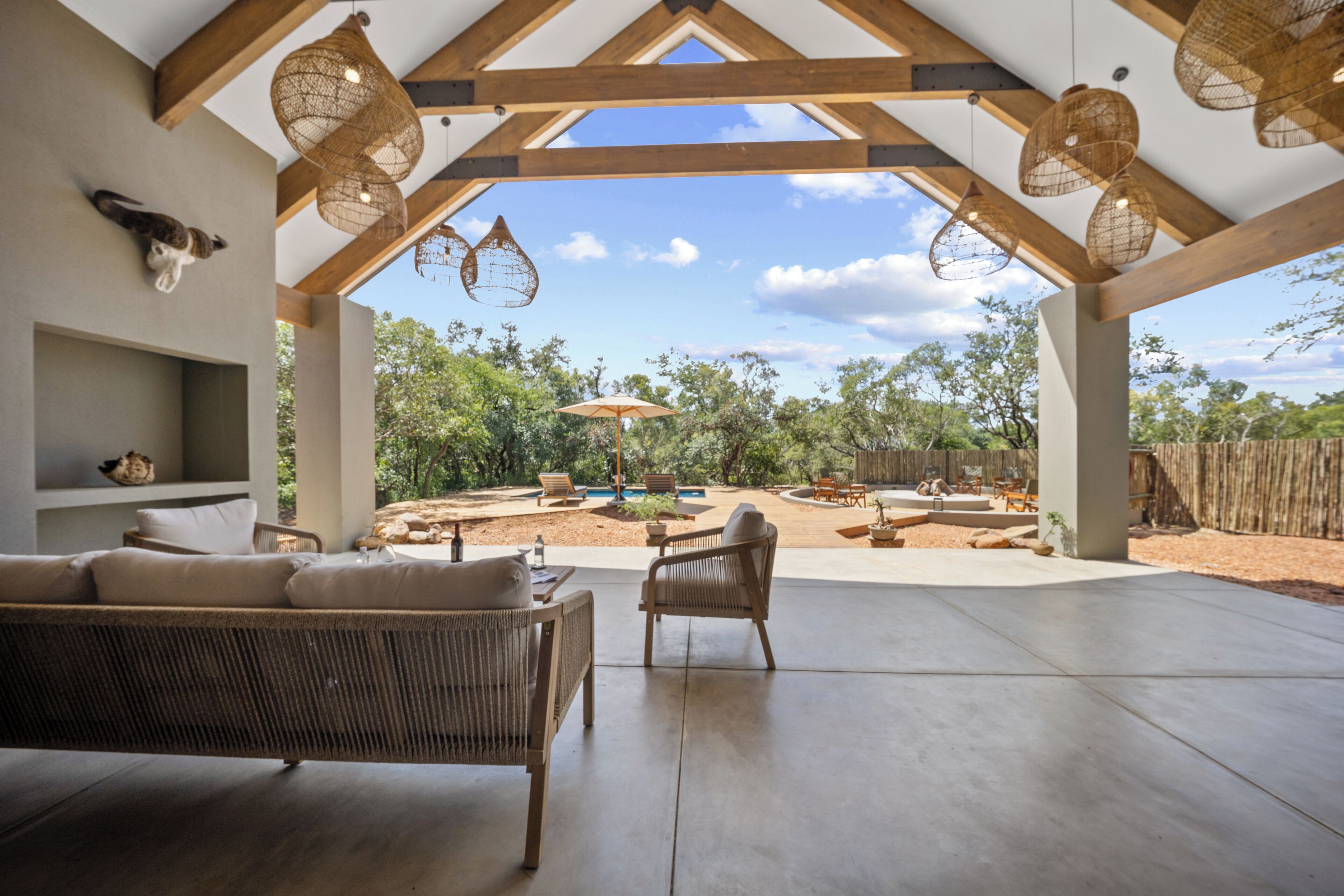 An open-plan living area with a view of a backyard, featuring a sofa, chairs, and hanging light fixtures.