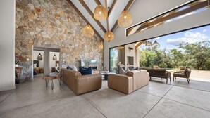 A spacious living area with stone walls, leather sofas, and a large glass door leading to an outdoor patio. - Kimbilia Luxury Villa  (Hoedspruit)
