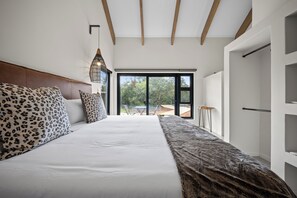 A bedroom with a large bed, a headboard, a hanging light fixture, and a view through a glass door. - Kimbilia Luxury Villa  (Hoedspruit)
