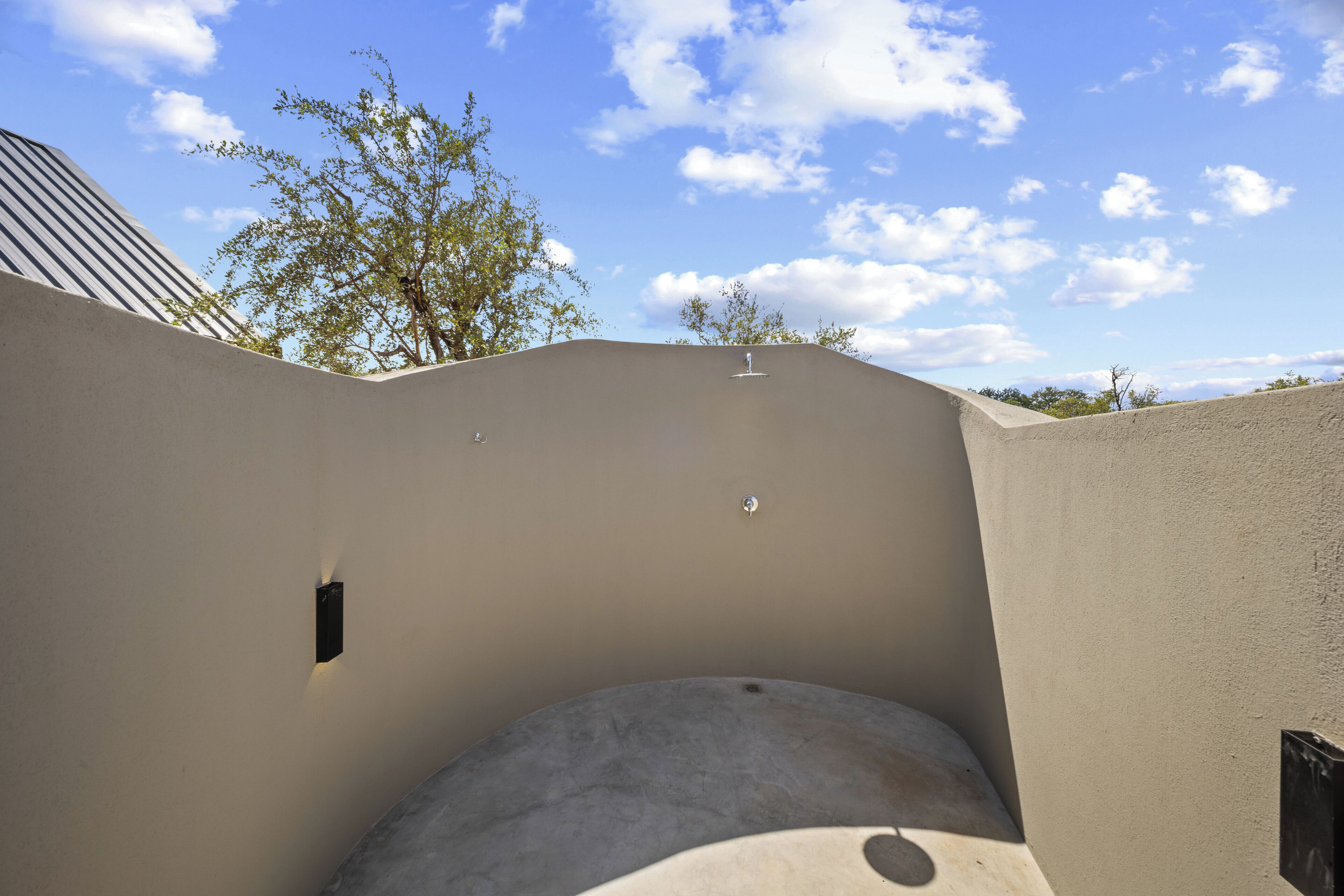 A curved wall with a recessed area, a small black object on the wall, and a tree in the background.