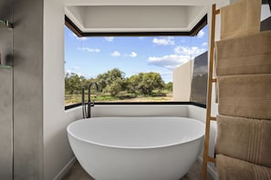 Un baño moderno con una bañera independiente, un ventanal con vistas a árboles y un perchero para toallas.
