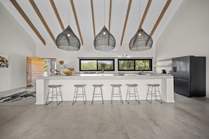 Una cocina moderna con una isla central, taburetes de bar, iluminación colgante y un refrigerador negro.