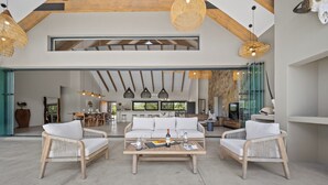 A spacious living area with a high ceiling, wooden beams, and wicker furniture. - Kimbilia Luxury Villa  (Hoedspruit)