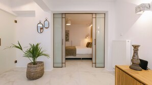 Moderni hotellihuone, jossa on sänky, yöpöytä, patteri ja ruukussa oleva kasvi.