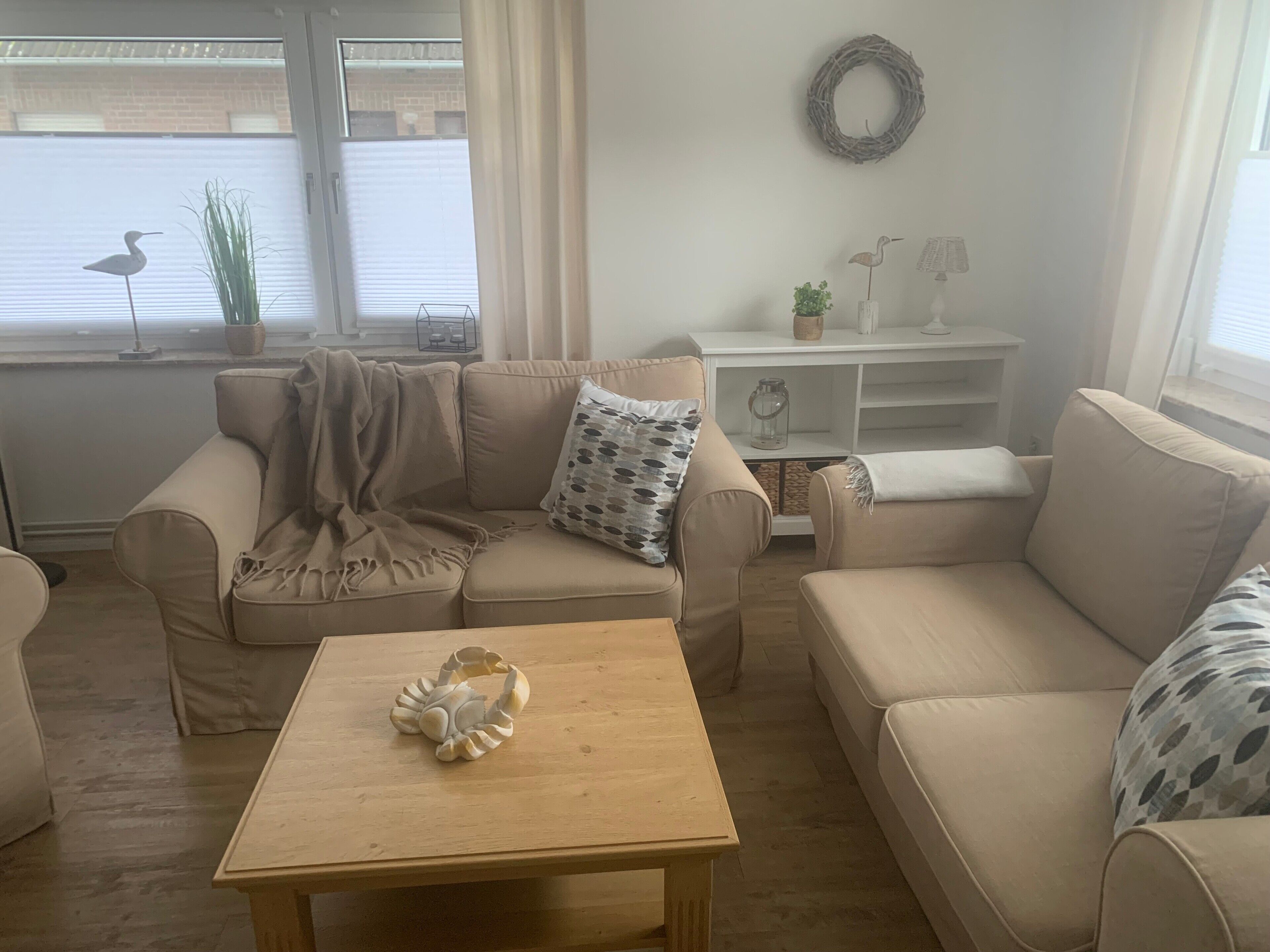 Un salon avec un canapé beige, une table basse en bois et un mur blanc orné d’une guirlande.