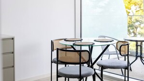 Et moderne spiseområde med runde glasborde og sorte metalstole, store vinduer med udsigt til træer.