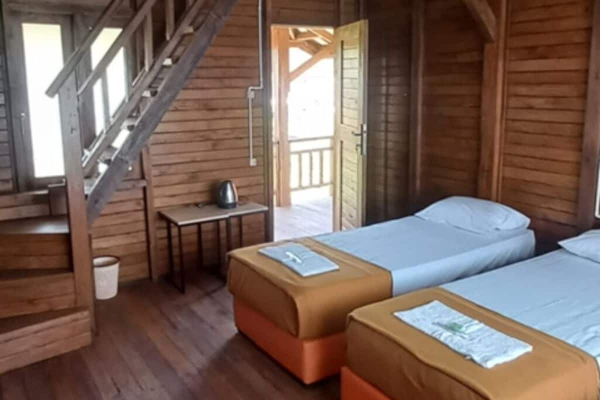 Ein Zimmer in einer Holzhütte mit zwei Betten, einem kleinen Tisch, einem Stuhl und einer Treppe.