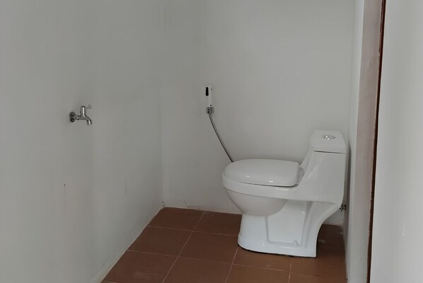 A small, white bathroom with a toilet, a wall-mounted faucet, and a visible electrical outlet.
