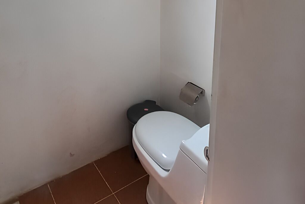 Un baño pequeño y funcional con un inodoro blanco, un cubo de basura y un dispensador de papel higiénico en la pared.
