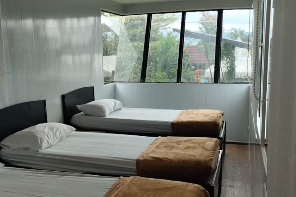 Ein Zimmer mit zwei Betten, einem Fenster mit Blick auf Grünflächen und einem Holzboden.