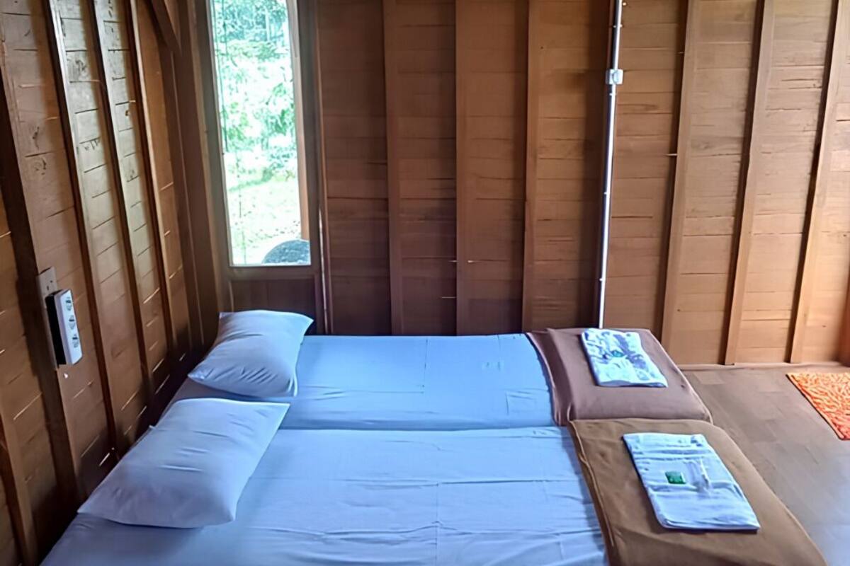 Ein Zimmer mit Holzboden, zwei Betten, einem Fenster und einer Holztür.