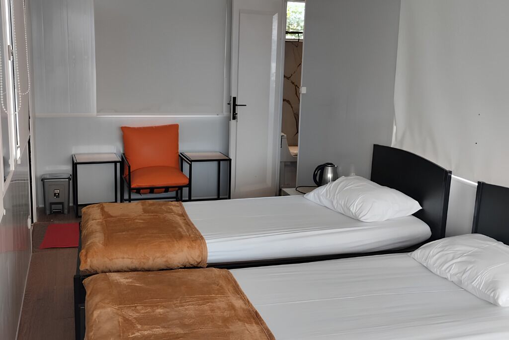 A hotel room with two beds, a chair, a small table, and a red rug.