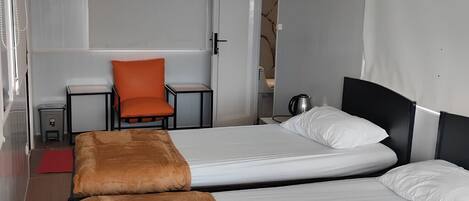 A hotel room with two beds, a chair, a small table, and a red rug.
