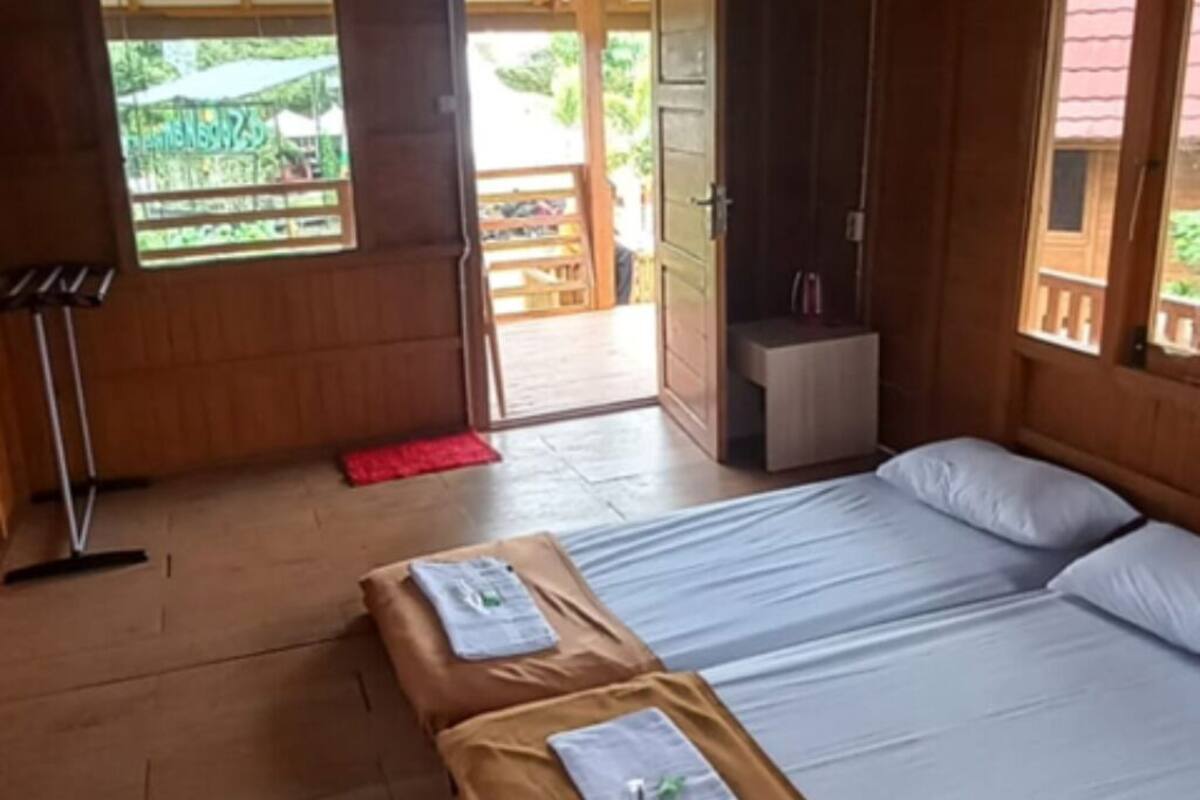 Ein Zimmer mit Holzboden, zwei Betten, einem kleinen Tisch und einer Tür zu einem Außenbereich.
