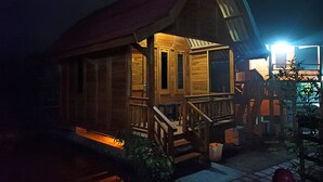 A wooden cabin with a porch, steps, and a small table. - Cozzy D'Sobahan Resort (Ngadirejo)