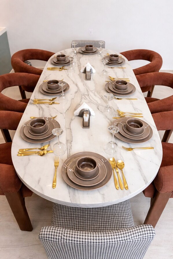 A dining table set with plates, bowls, and cutlery, surrounded by upholstered chairs. - Liora Jubaila Resort (Diryah)