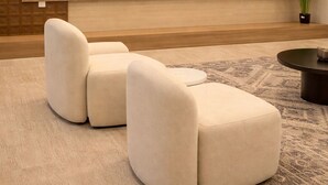 Een moderne woonkamer met een flatscreen televisie aan de muur, een beige bank, een salontafel en een kamerkleed met een patroon.