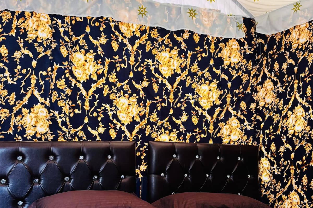 A bedroom with a tufted headboard, a patterned wall, and a tent-like ceiling structure.