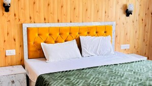 Una cama con cabecera amarilla, almohadas blancas y manta verde.