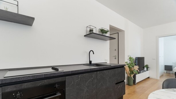 Une cuisine moderne dotée d’un plan de travail noir, d’un four encastré et d’un robinet noir.