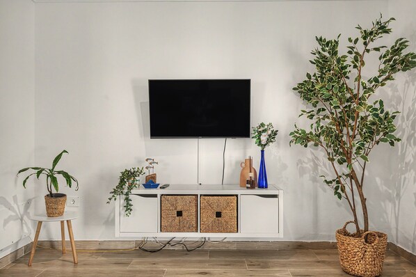A modern living room with a flat-screen TV mounted on a white cabinet, a potted plant, and a wicker basket.